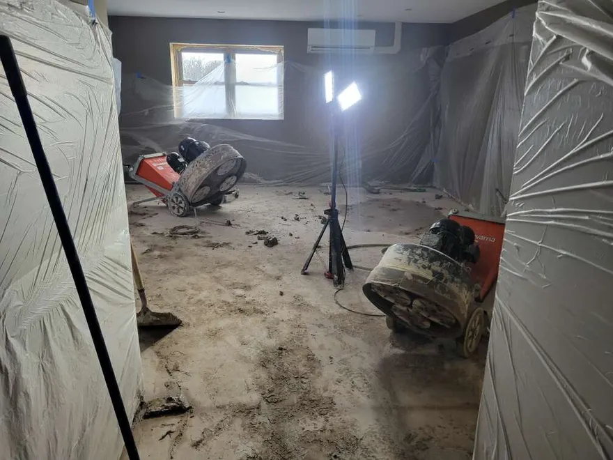 Concrete grinding equipment preparing a basement floor with dust containment in place